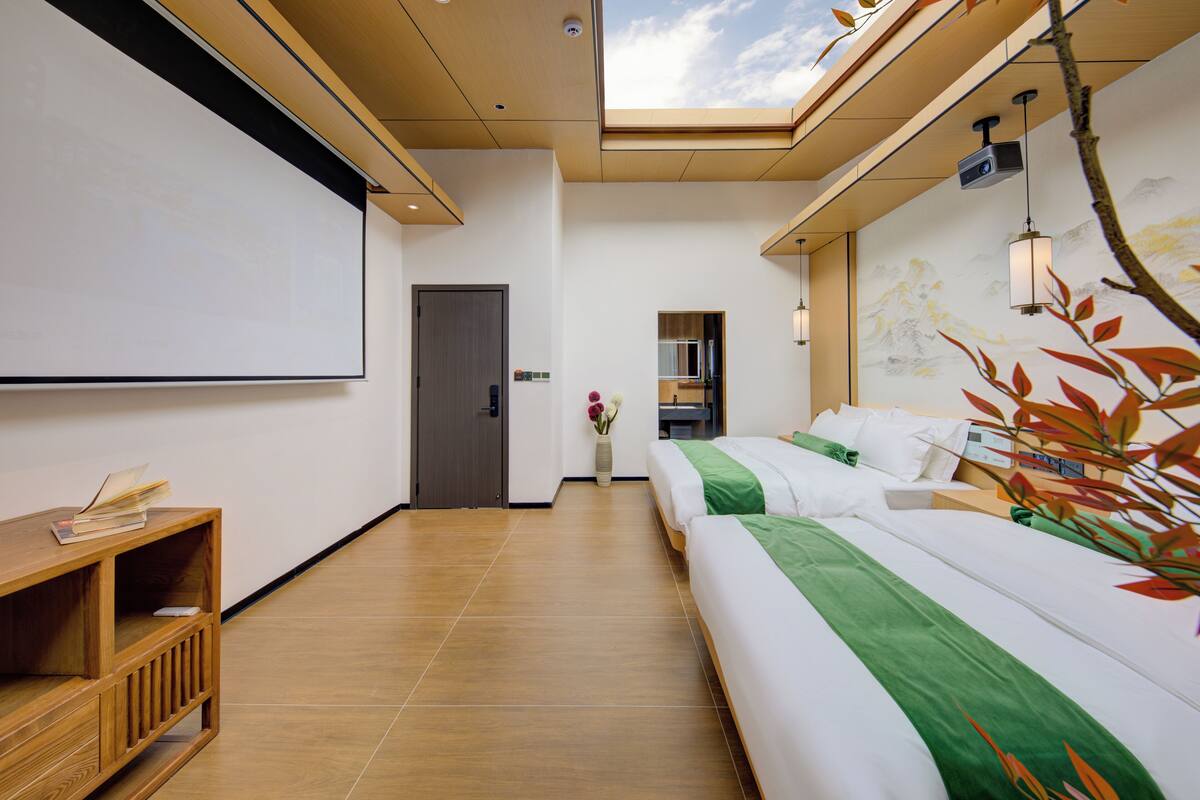 Habitación de hotel con cama, escritorio, pantalla de proyector y tragaluz.