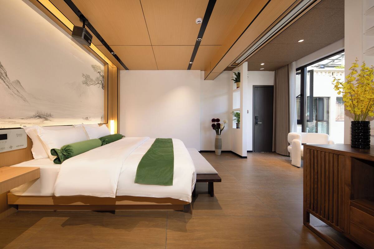 Una habitación de hotel moderna con una cama grande, una mesita de noche y vistas de la ciudad a través de amplias ventanas.