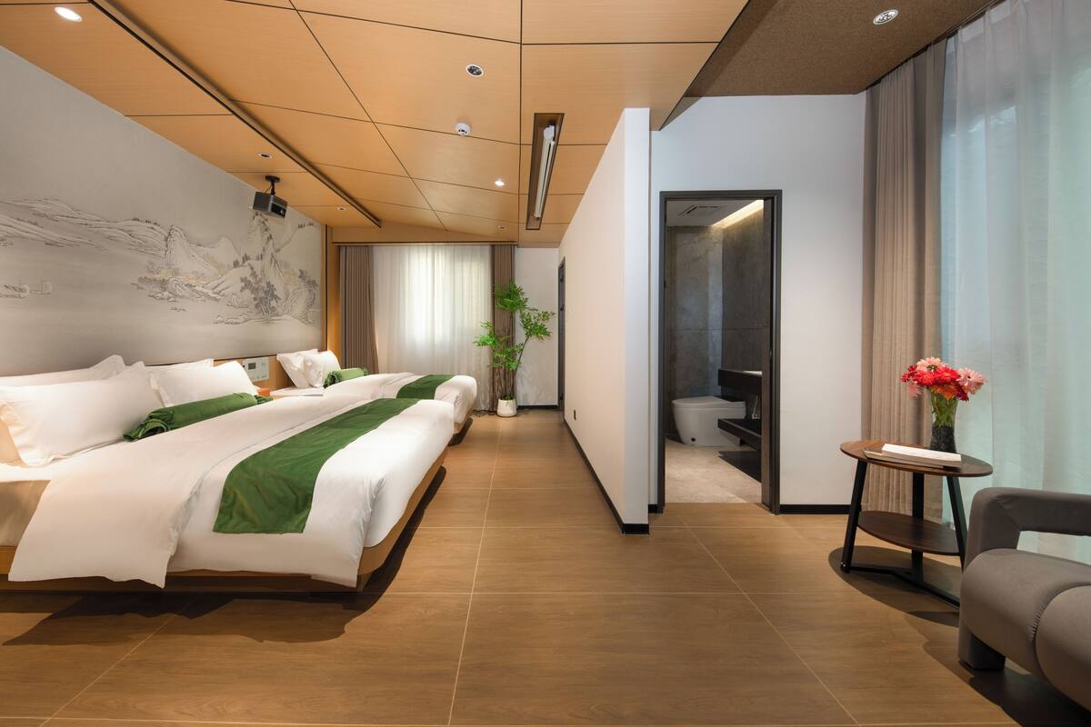 Una habitación de hotel moderna con una cama grande, un pequeño rincón de descanso y un baño a la vista a través de una puerta abierta.