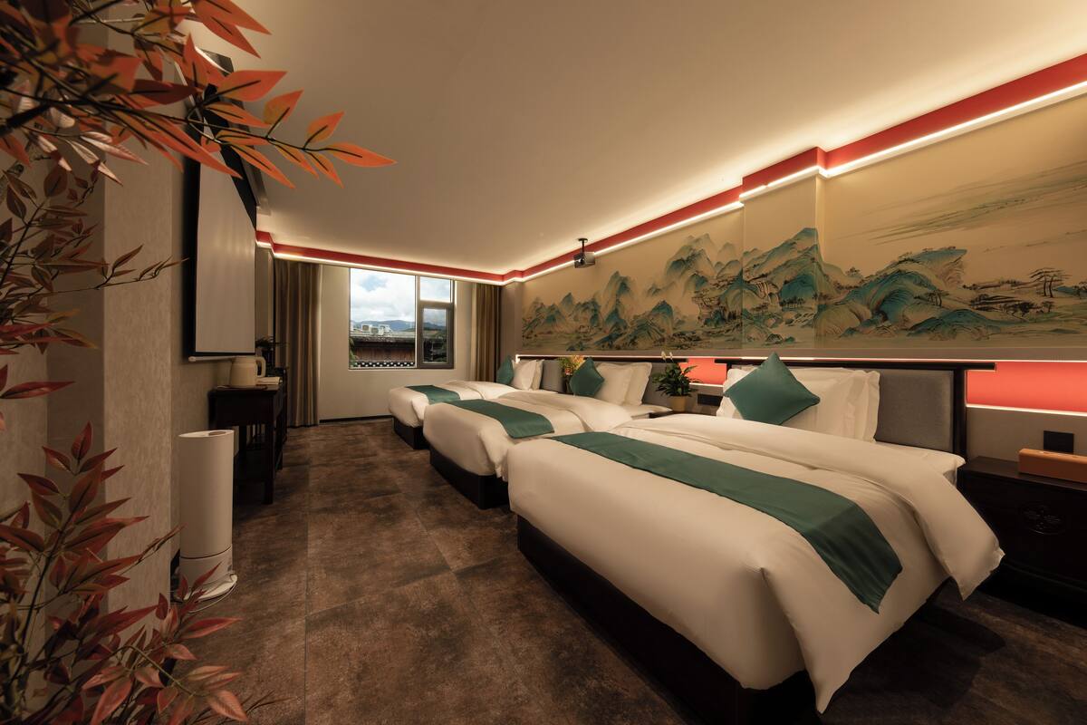 Una habitación de hotel con una cama grande, una cama más pequeña, un escritorio y un cuadro en la pared.