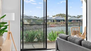A modern living room with a large sliding glass door leading to a balcony with a view of houses and a body of water. - Waterside Victor Harbor (Victor Harbor)