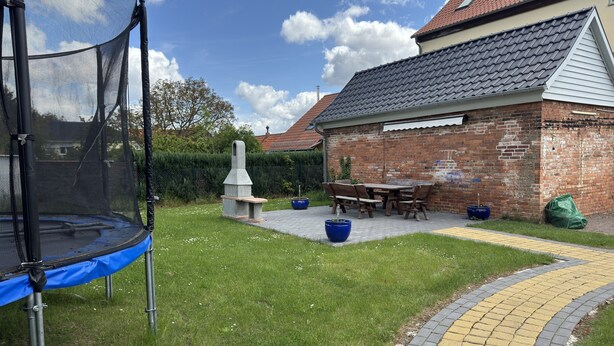 Un jardin avec un trampoline, un barbecue et une terrasse en briques.