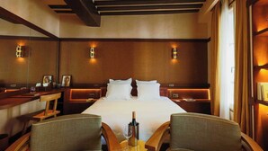 A hotel room with a large bed, two bedside tables, a wooden chair, a small round table with a bottle and glass, and wall-mounted lights. - Confidential Room 1, a Stone's Throw From the Louvre (Paris)