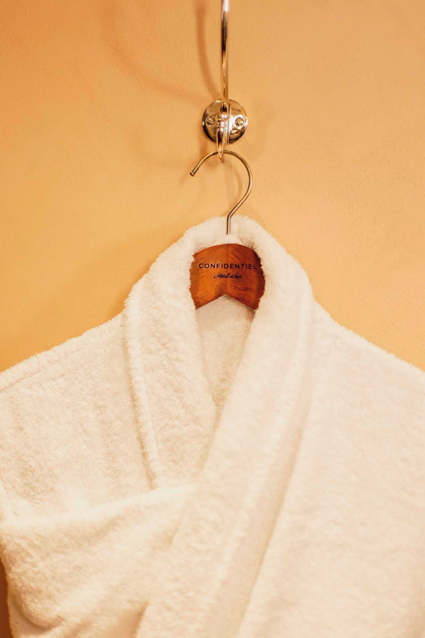 A white bathrobe hanging on a wooden hanger with a metal clip.