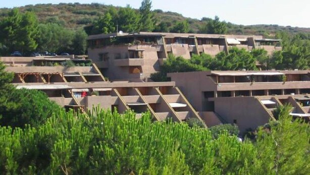 A multi-story building with a flat roof and balconies, surrounded by greenery and hills. - Apartment in Sardinia With Sea View (Olbia)