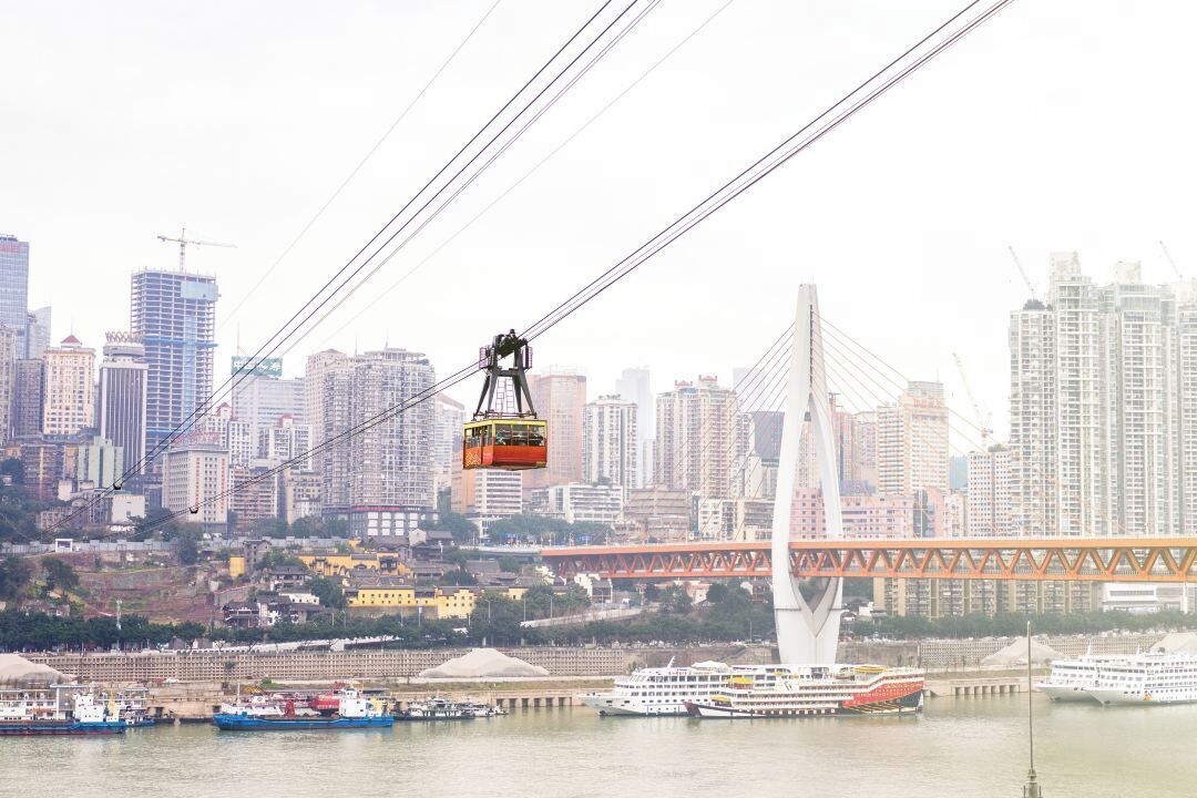 Un téléphérique traversant une rivière, avec un pont et le profil de la ville en arrière-plan.