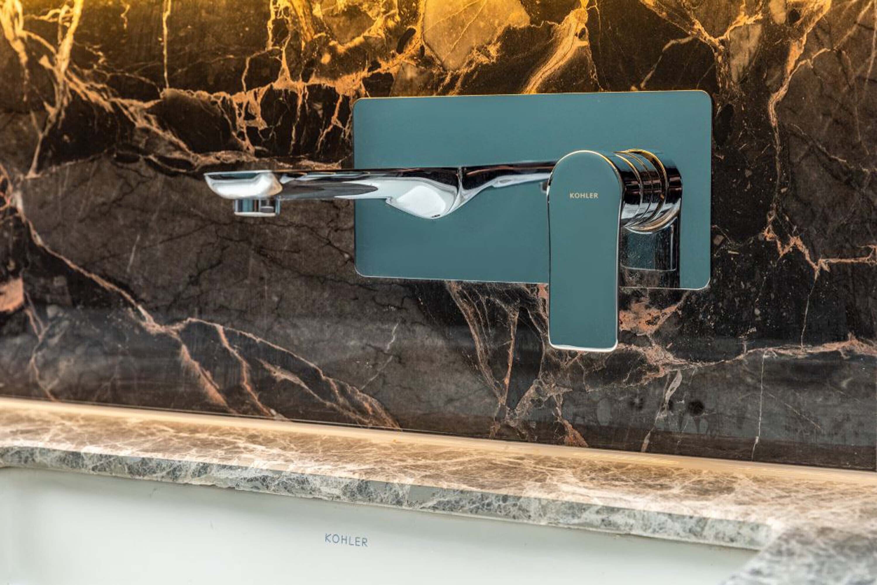 Een moderne badkamer met een marmeren spatwand en een Kohler-kraan gemonteerd op een blauwgroene paneel.