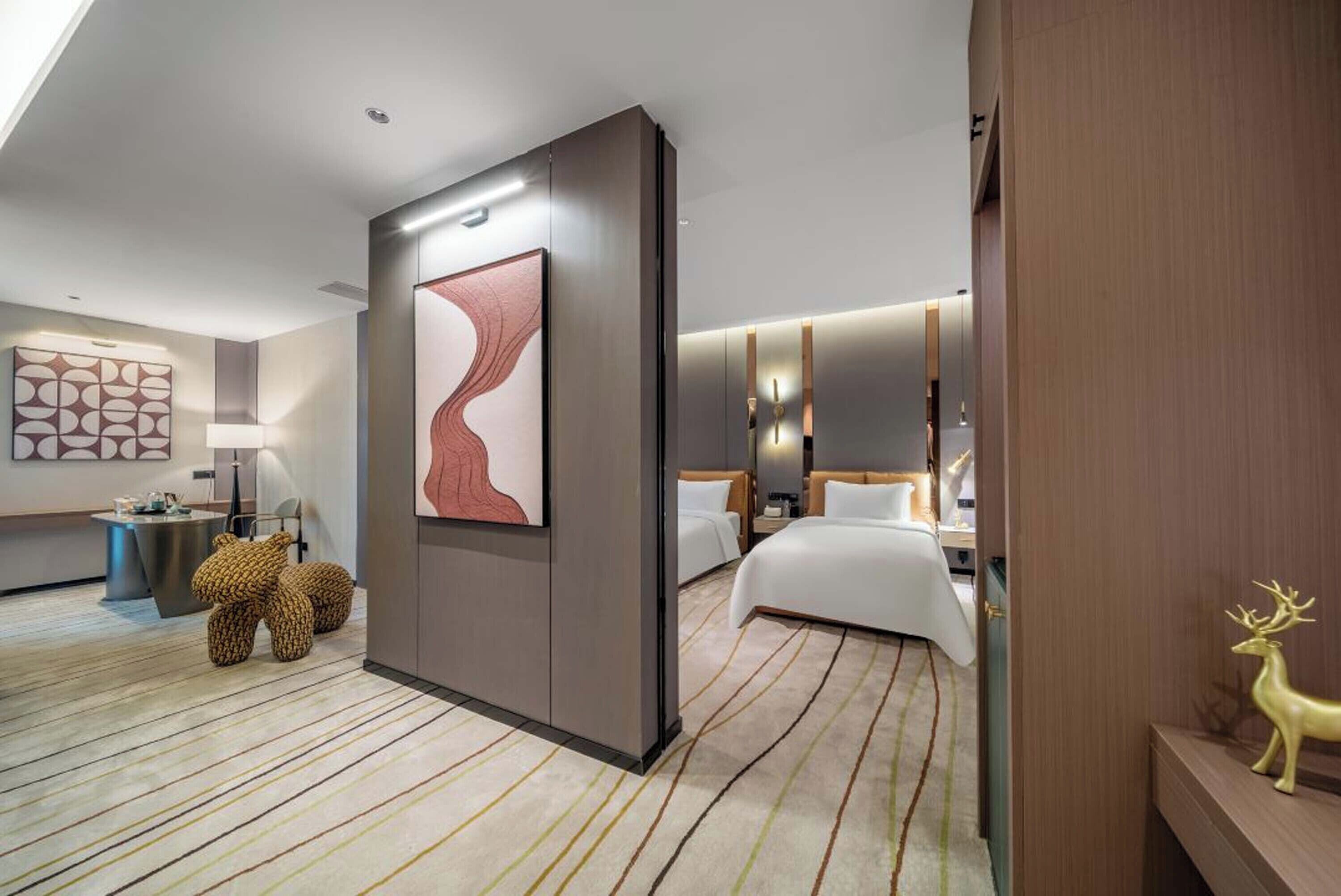 A modern hotel room with a large bed, a bedside table, a lamp, and a decorative wall piece.