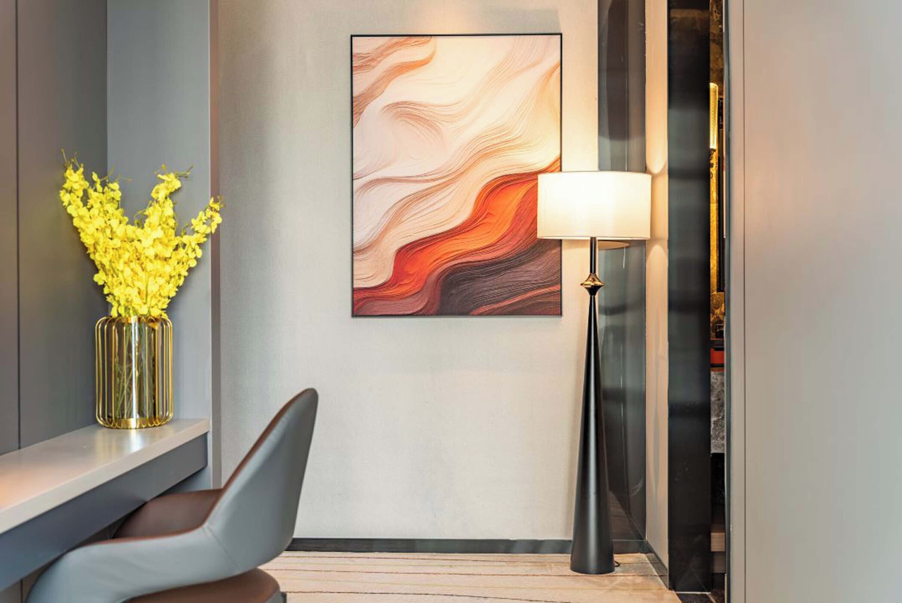 Een modern interieur met een grijze muur, een lijst met abstract schilderij, een vaas met gele bloemen, een lamp en een stoel.