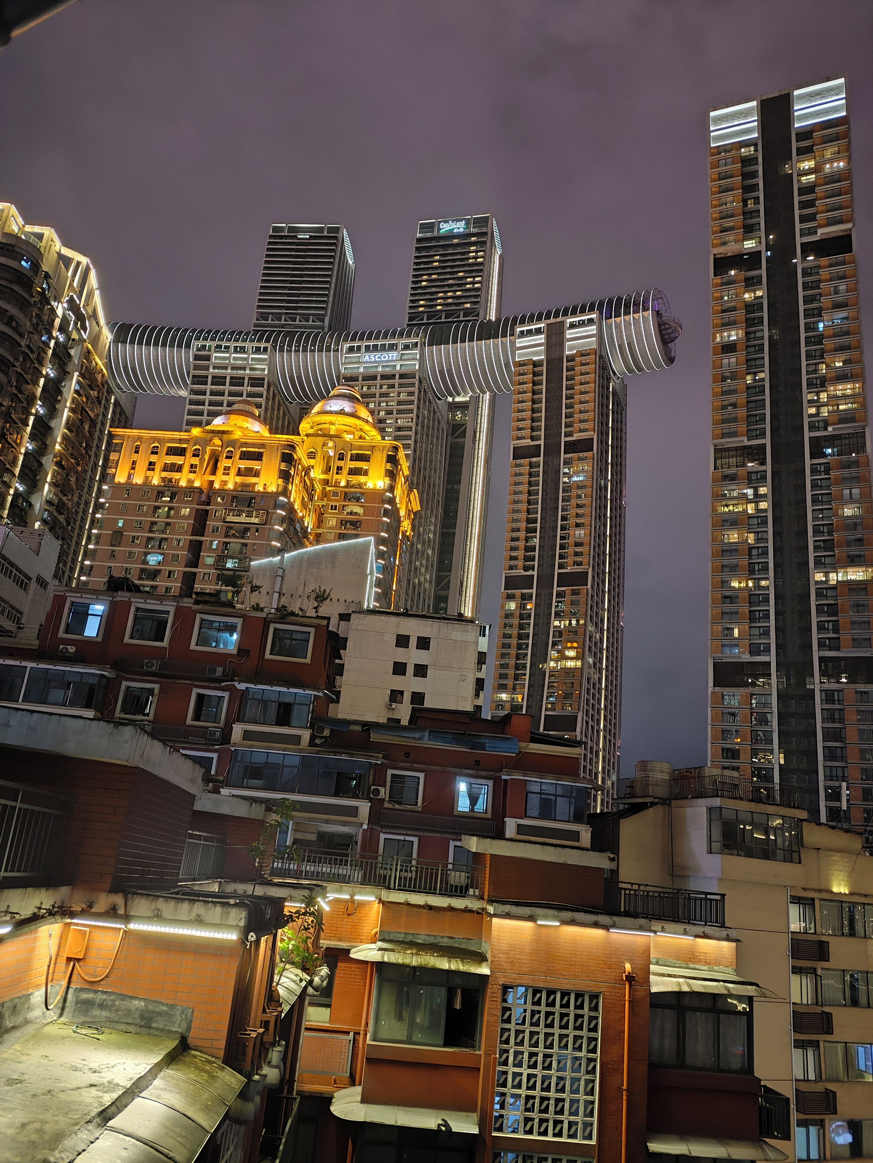 A high-rise building with multiple balconies and a distinctive yellow-lit structure in the center.