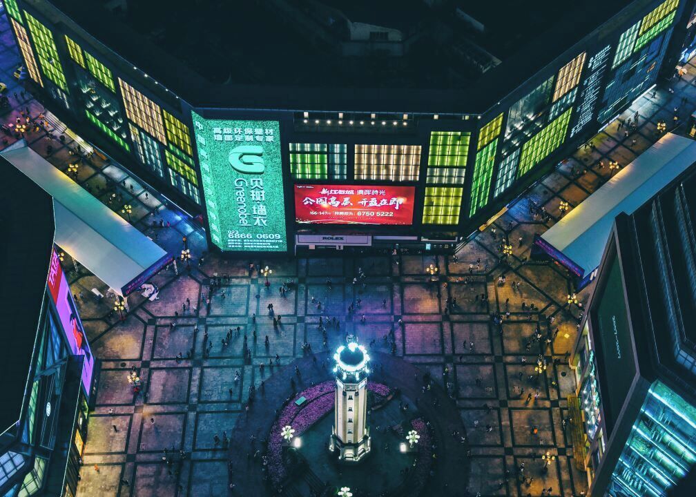 A modern building with multiple illuminated signs and a central circular plaza with a fountain.