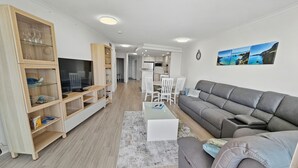 Una sala moderna con un sofá gris, mueble de entretenimiento de madera y una zona de comedor con sillas blancas.