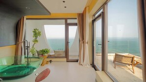 A modern bathroom with a glass bathtub, a potted plant, and a view of the sea through large windows. - Yasong Jianwen Resort Hotel (Qingdao)