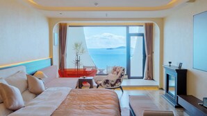A modern hotel room with a large bed, a seating area with a chair, a TV, and a view of the sea. - Yasong Jianwen Resort Hotel (Qingdao)