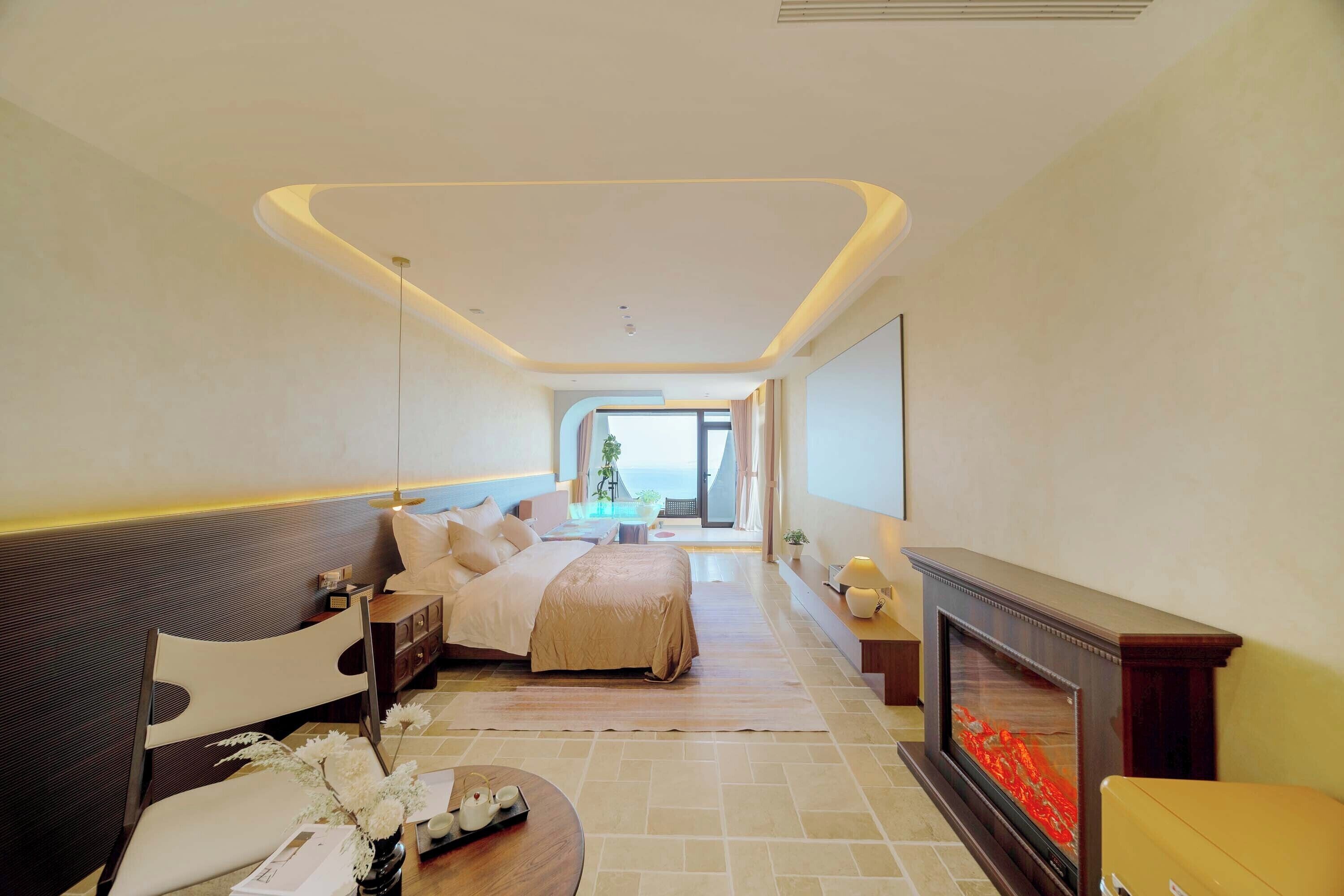 A modern hotel room with a bed, a sofa, a fireplace, and a view of the sea.