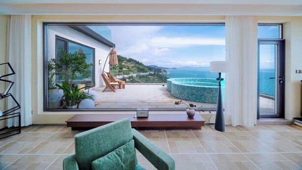 A spacious living area with a large window overlooking a pool and scenic views. - Yasong Jianwen Resort Hotel (Qingdao)
