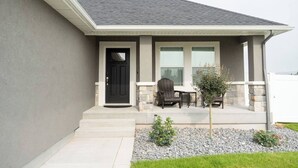 A residential house with a dark front door, a small porch with two chairs and a table, and a stone wall.