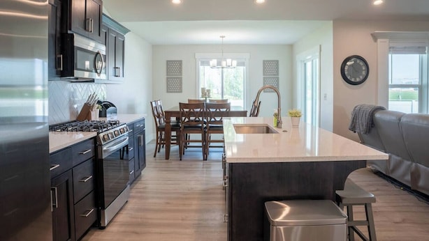 A modern kitchen with dark cabinetry, a central island, and a dining area with wooden chairs and a chandelier.