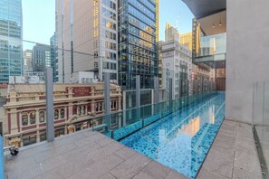 A rooftop pool with a glass barrier, overlooking a cityscape with modern and historic buildings. - Sydney Luxe Observatory Home | City, Pool & Gym (Sydney)