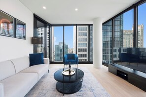 A modern living room with a sofa, a blue armchair, a glass coffee table, and a large window offering a city view. - Sydney Luxe Observatory Home | City, Pool & Gym (Sydney)