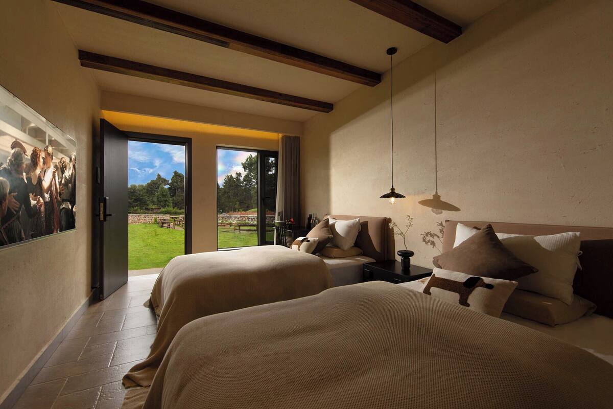 A hotel room with two beds, a large window, and a view of a garden.