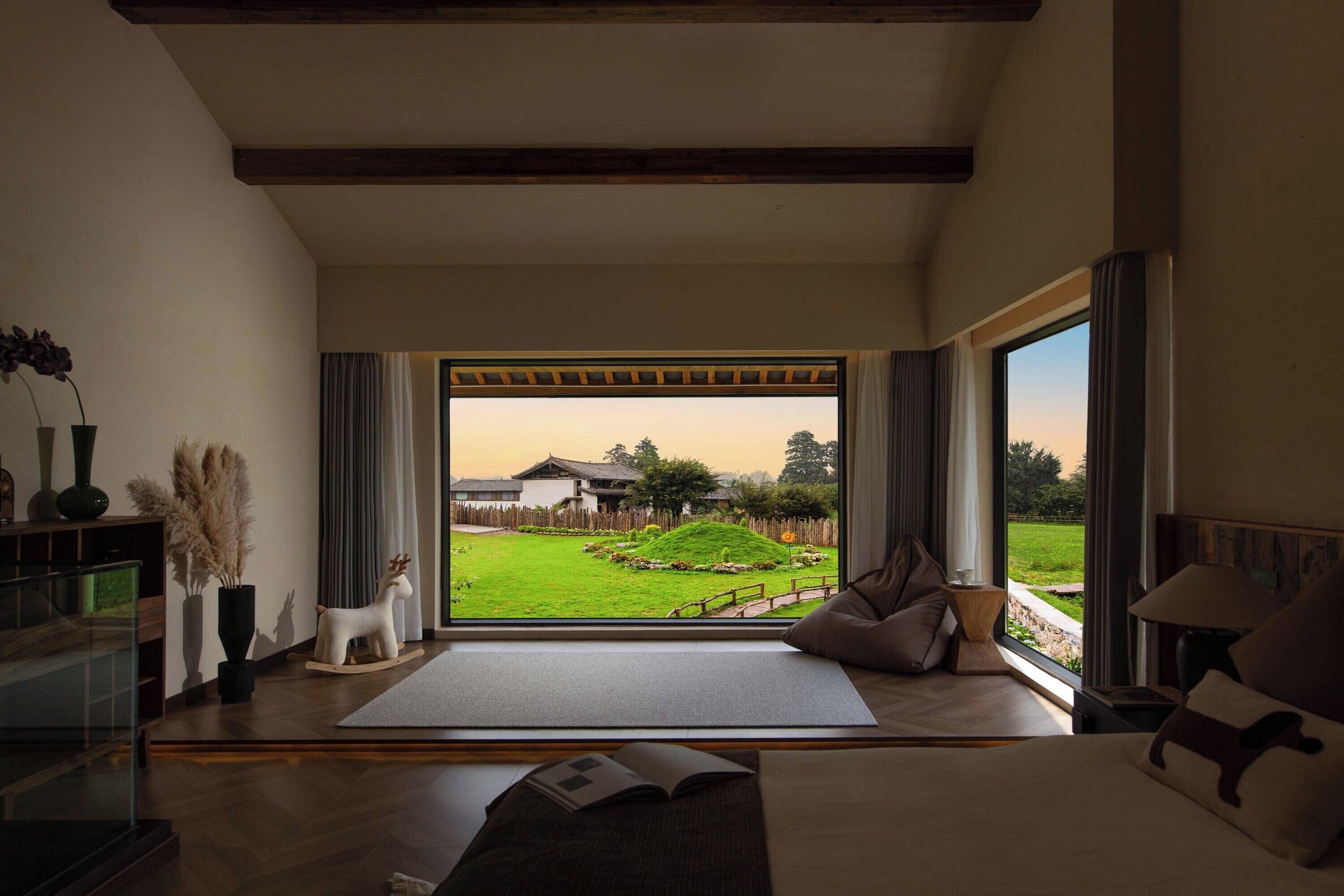 A hotel room with a large window offering a view of a garden and traditional buildings.