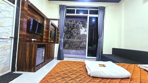 A room with a bed, a TV, a wooden cabinet, and a sliding glass door leading to a balcony. - Soham Resort Diveagar (Shrivardhan)
