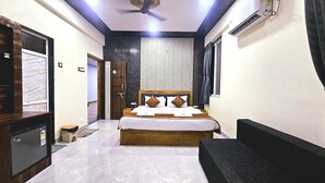 A hotel room with a bed, a TV, a ceiling fan, and a window with curtains. - Soham Resort Diveagar (Shrivardhan)
