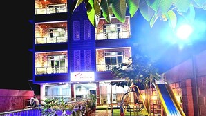 A multi-story building with a brick facade, a balcony, and a playground area with a slide. - Soham Resort Diveagar (Shrivardhan)