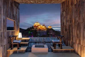 Una terraza de madera con asientos y vista a un edificio tradicional al anochecer.