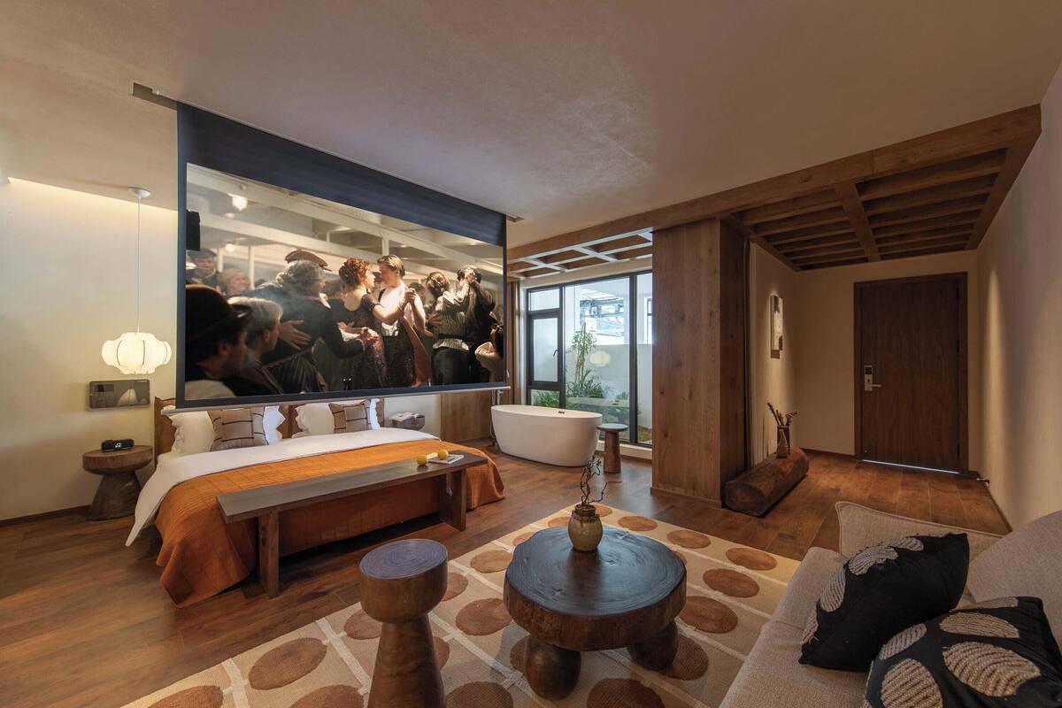 Une chambre d’hôtel moderne dotée d’un grand lit, d’un coin salon avec un canapé et une table basse, d’une baignoire et d’un grand miroir qui reflète la pièce.