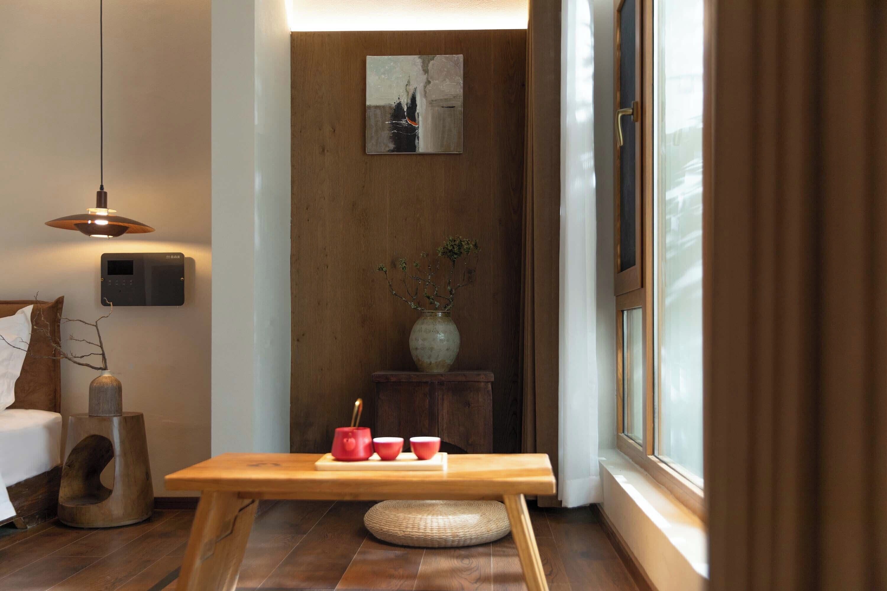 Una habitación moderna con piso de madera, una mesa de madera con un florero y tazas, un altavoz en la pared y una ventana con cortinas.