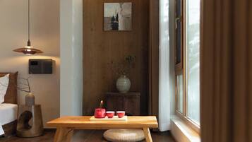Una habitación moderna con piso de madera, una mesa de madera con un florero y tazas, un altavoz en la pared y una ventana con cortinas.