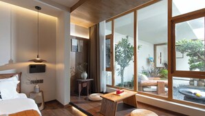 Een moderne hotelkamer met een groot raam, een houten vloer, een bed, een nachtkastje en een zithoekje.
