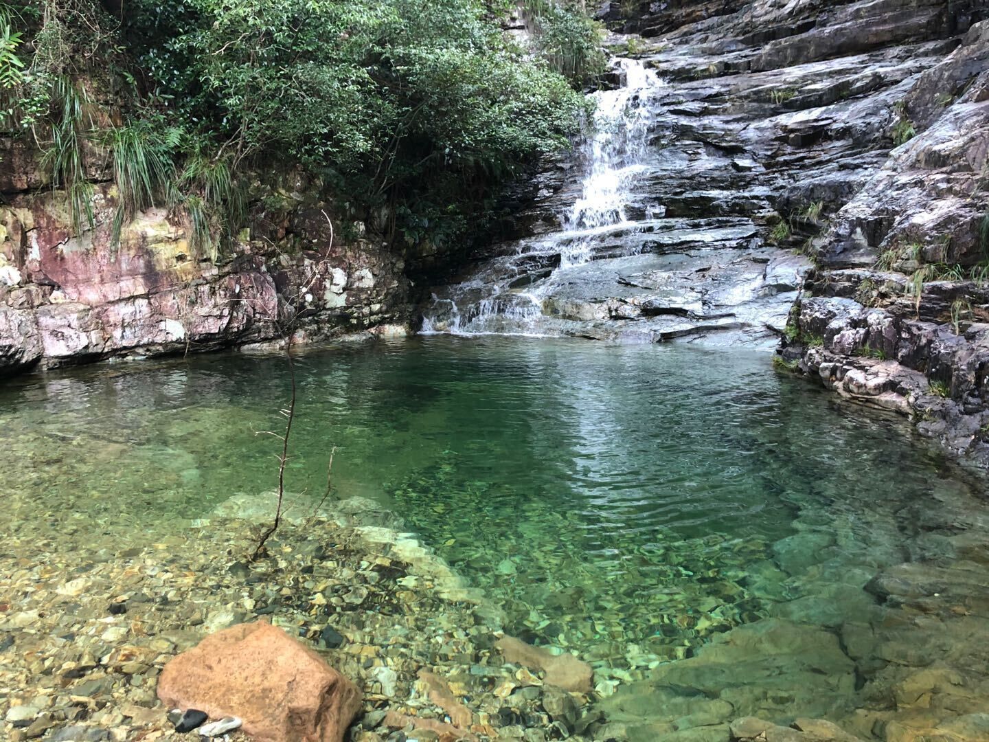 Une cascade aux eaux claires, tombant en cascade sur des rochers, et se déversant dans un bassin entouré d’une végétation luxuriante.