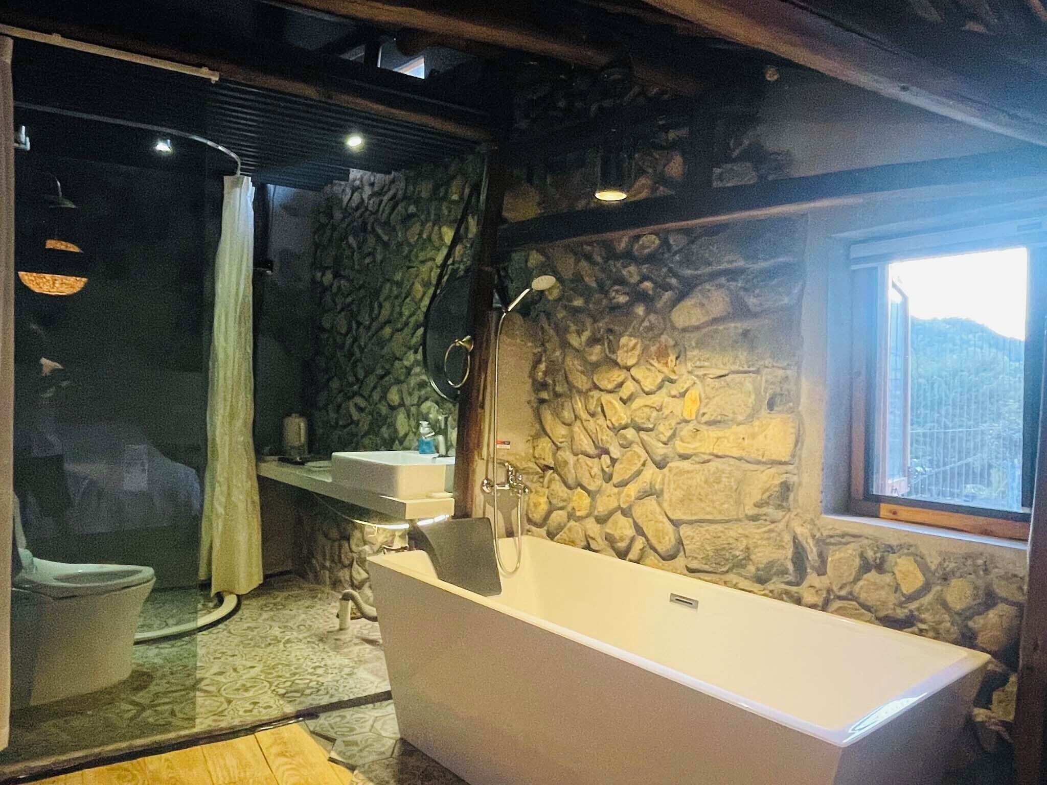 A bathroom with a stone wall, a bathtub, a sink, and a window.