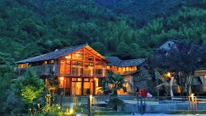 A large, modern house with a glass facade, surrounded by lush greenery and hills. - Lishui Manshanju Forest Retreat (Lishui)
