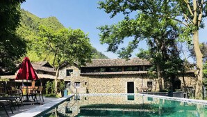A stone building with a swimming pool, outdoor seating, and a red umbrella. - Lishui Manshanju Forest Retreat (Lishui)
