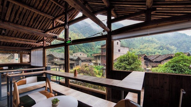 A rustic wooden interior with a view of traditional houses and mountains. - Lishui Manshanju Forest Retreat (Lishui)