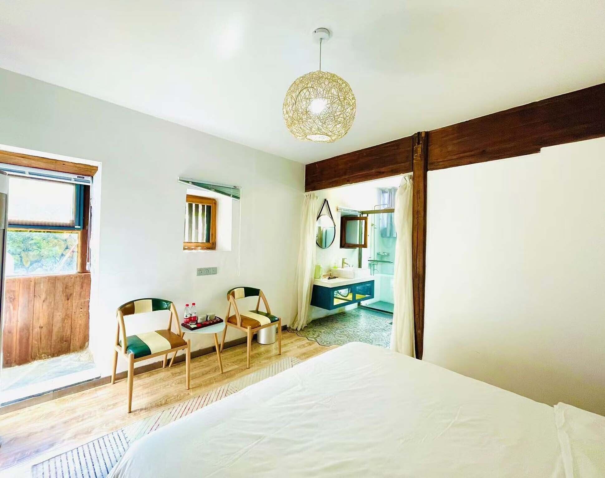 A bedroom with a bed, two chairs, a desk, a mirror, and a bathroom visible through an open door.