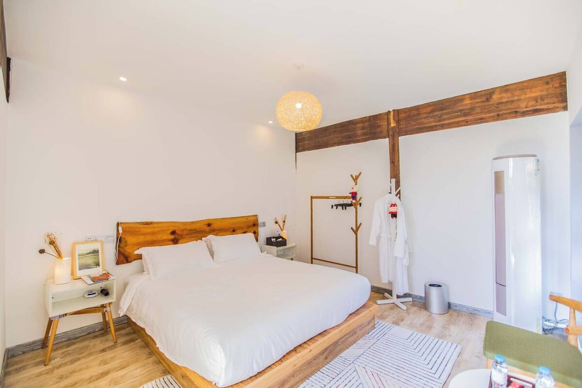 A modern bedroom with a wooden headboard, a bed with white linens, a bedside table with a lamp, and a large mirror.