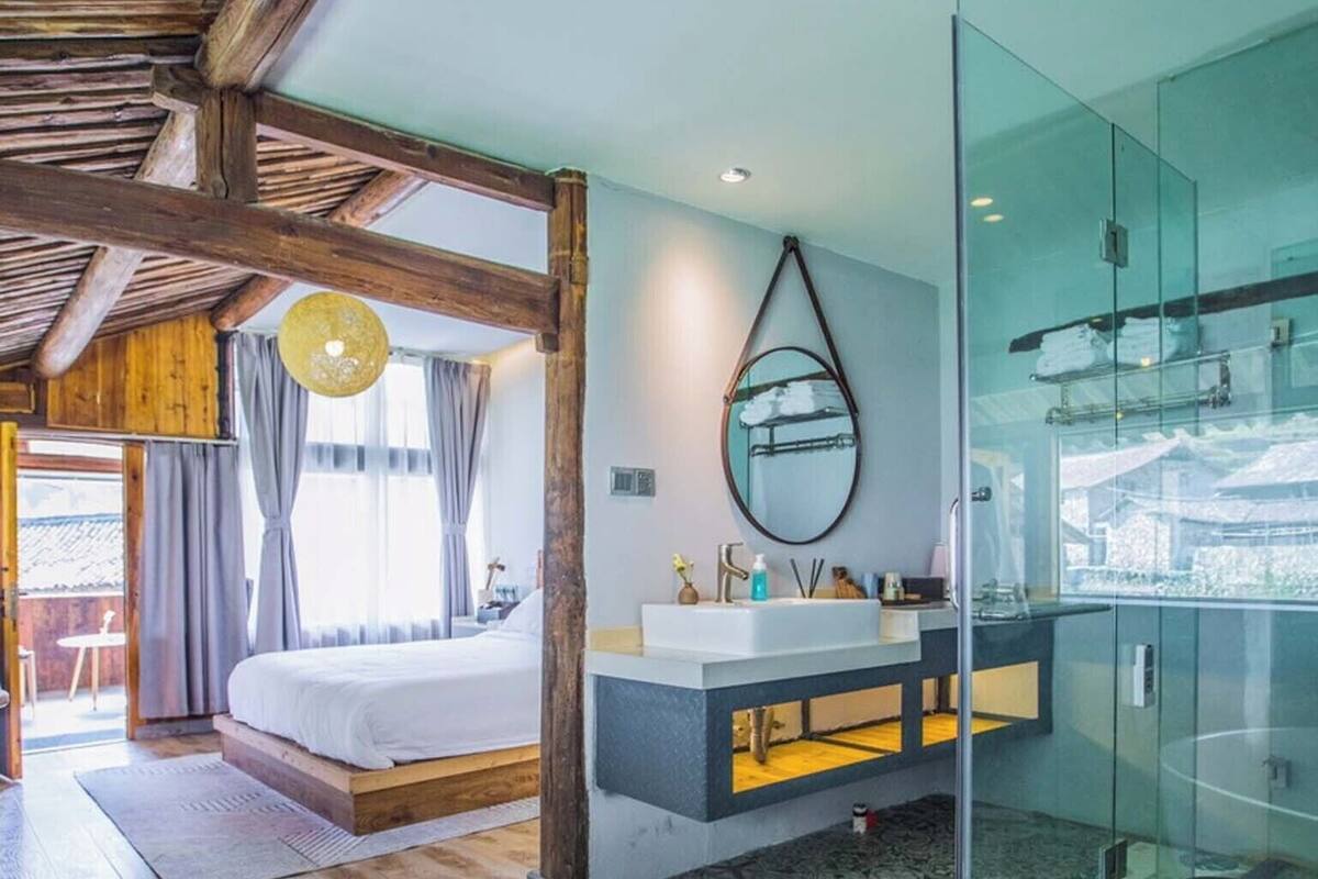 A modern bedroom with a large bed, a glass-enclosed shower, and a visible balcony.