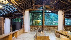 A rustic wooden interior with a stone wall, a flat-screen TV, a woven table, and a stone bench. - Lishui Manshanju Forest Retreat (Lishui)