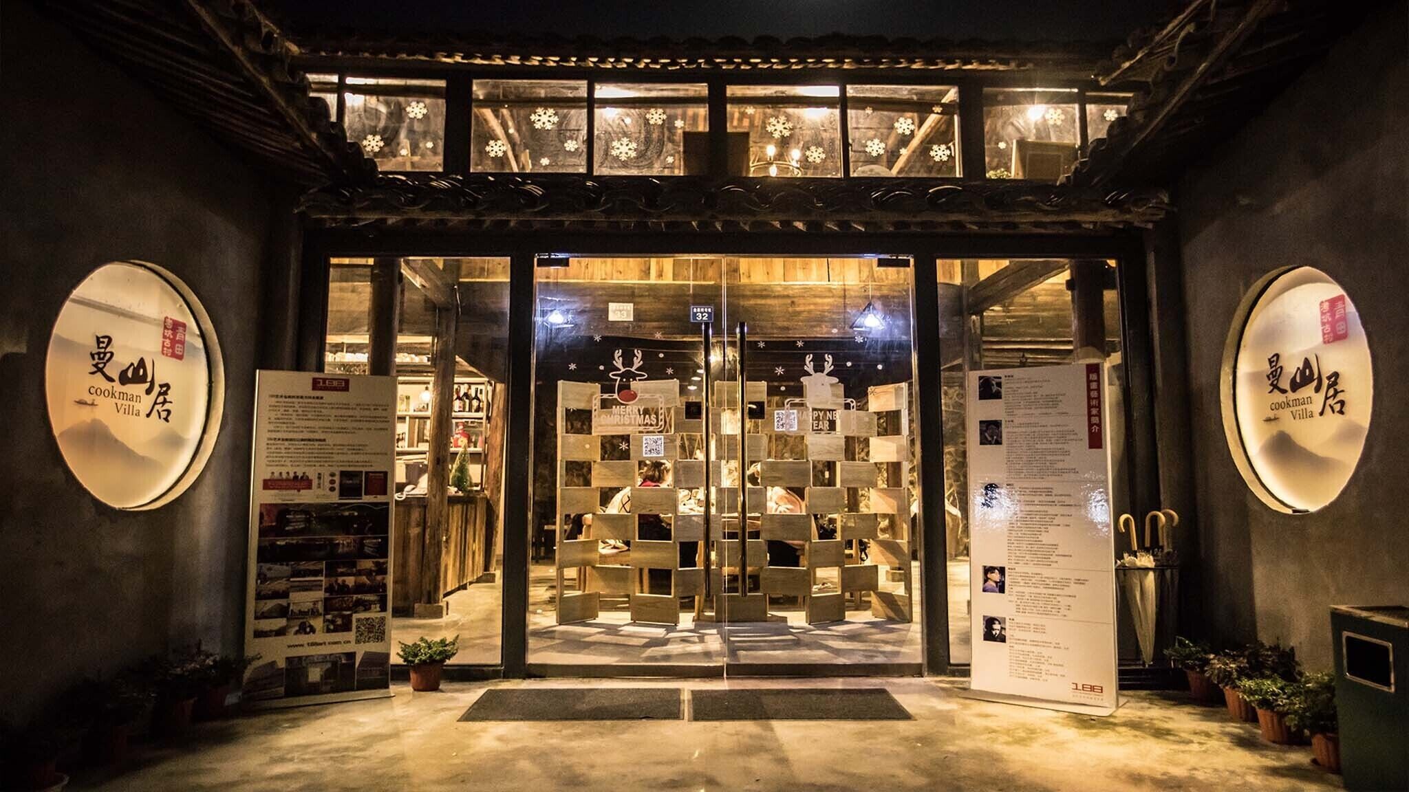 A restaurant entrance with a wooden lattice door, illuminated signs, and a menu board.