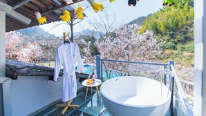 A spa area with a large bathtub, a glass table with drinks, and a white robe hanging. - Lishui Manshanju Forest Retreat (Lishui)