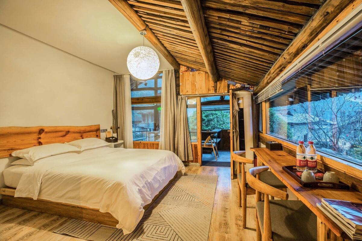 A wooden room with a bed, a desk, and a view of the outdoors.