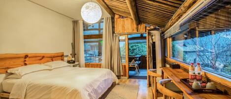 A wooden room with a bed, a desk, and a view of the outdoors.