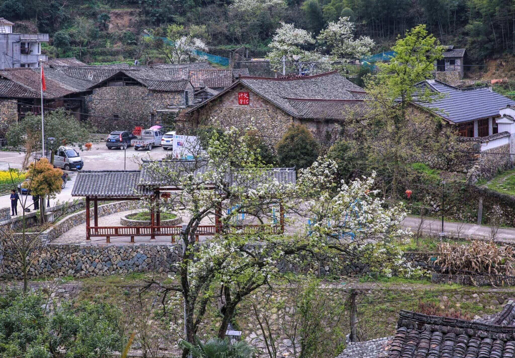 A traditional village with stone buildings, a central pavilion, and a stone wall.