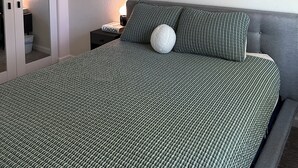 Ein Schlafzimmer mit einem Bett, einem Deckenventilator, einem Nachttisch mit Lampe und zwei abstrakten Bildern an der Wand.