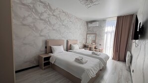 A modern hotel room with two beds, marble-patterned walls, a wooden floor, a flat-screen TV, and an air conditioning unit.